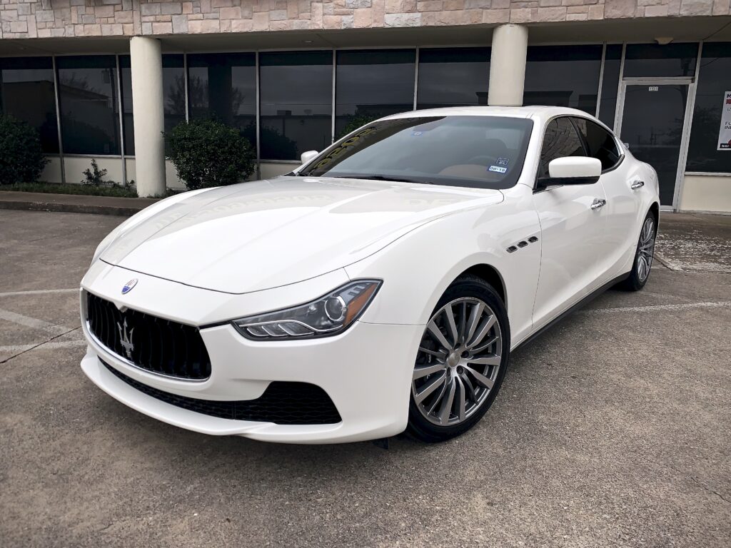 A white Maserati parked in front of a dealership.