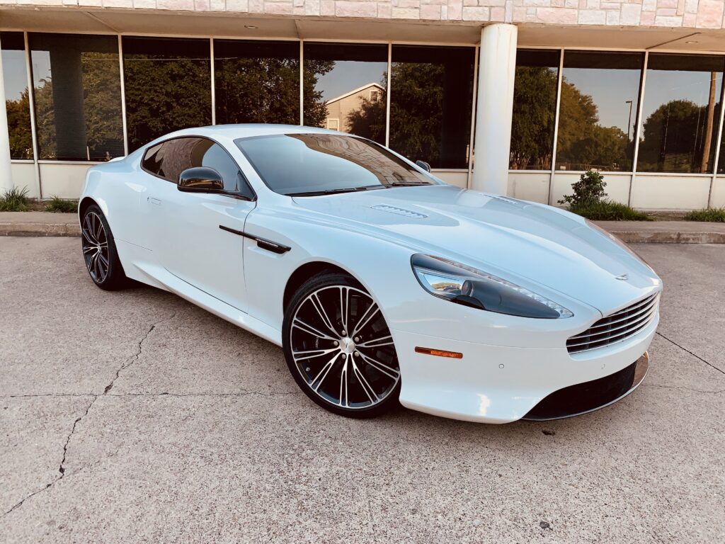 A white Aston Martin parked in front of a dealership.