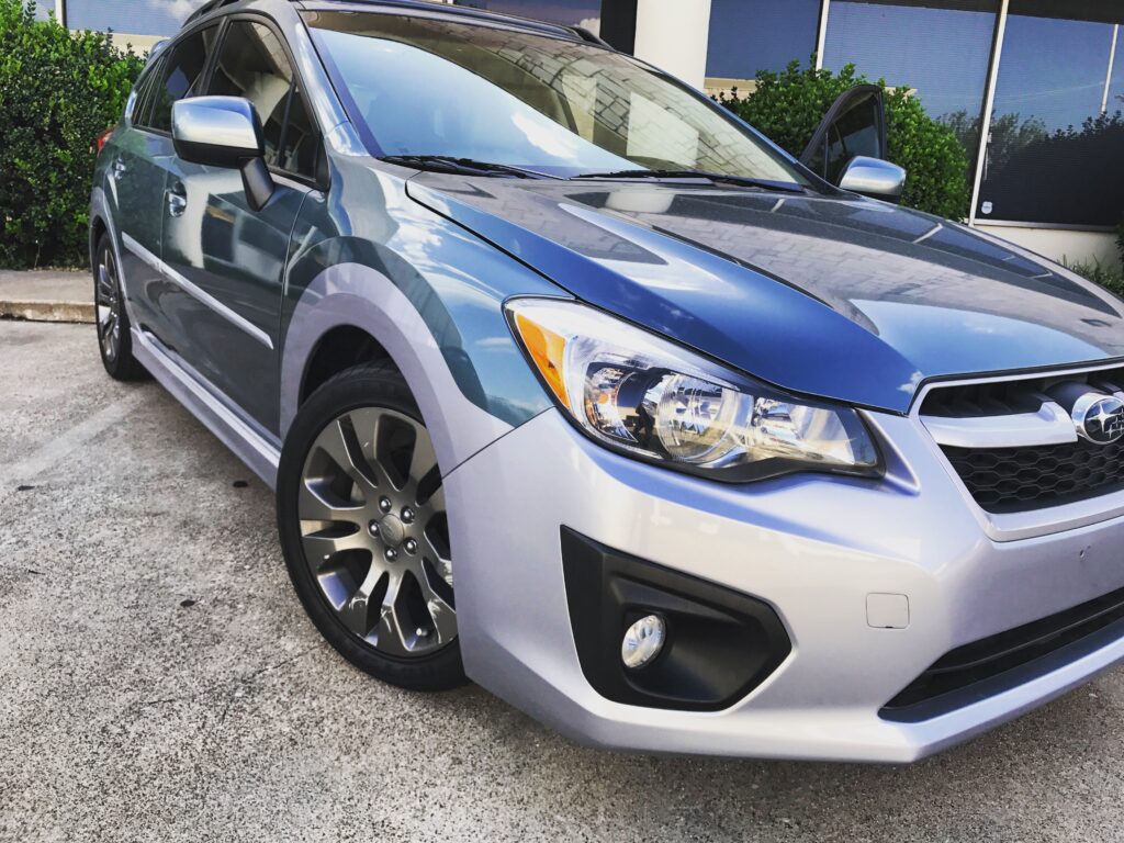 A blue and silver Subaru hatchback model parked at an angle in front of a dealership.