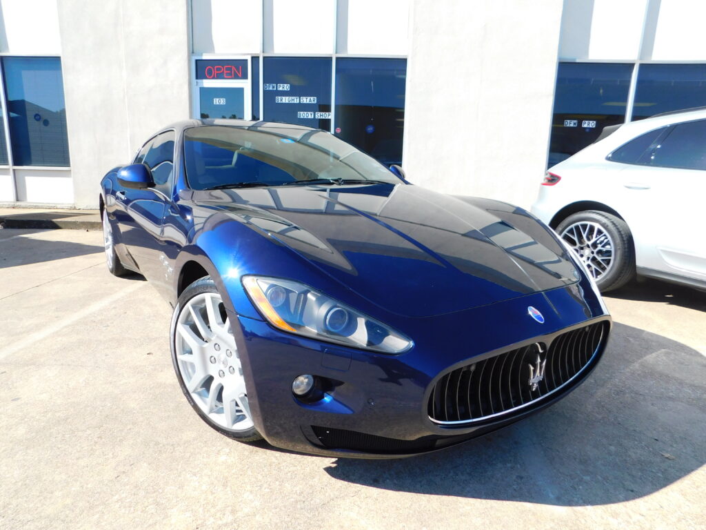 A blue Maserati parked in a lot in front of a dealership.