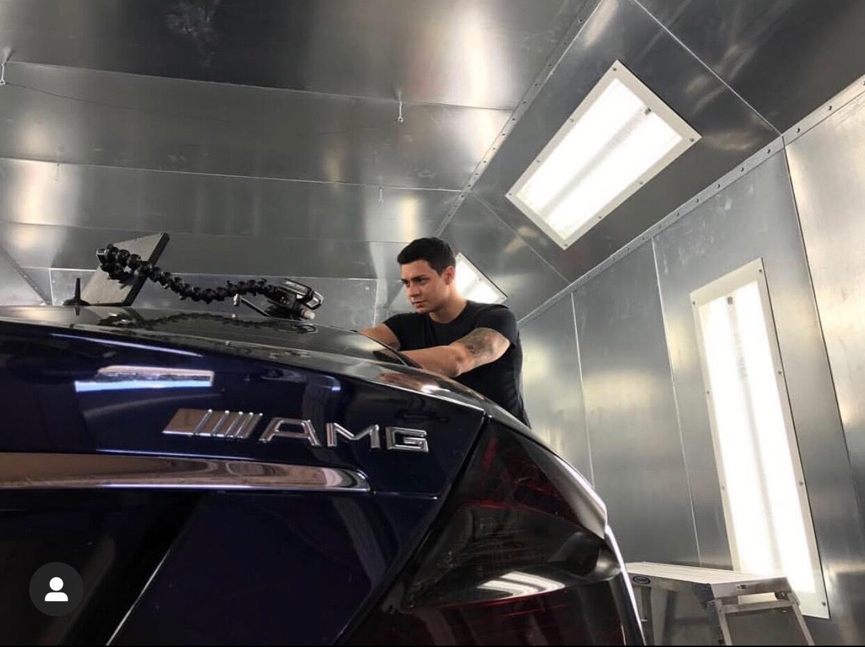 A body shop technician repairing hail damage to a black car.
