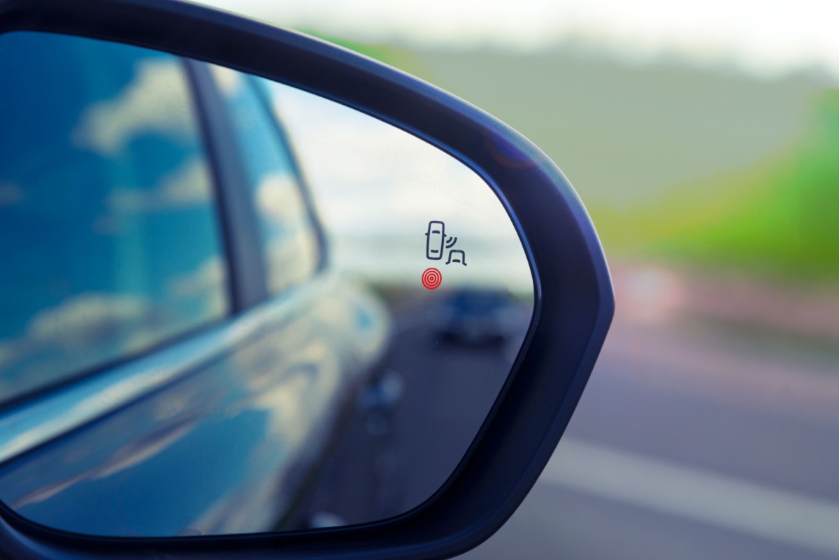 A close-up of a car's rearview mirror, which feature blind-spot monitoring sensors